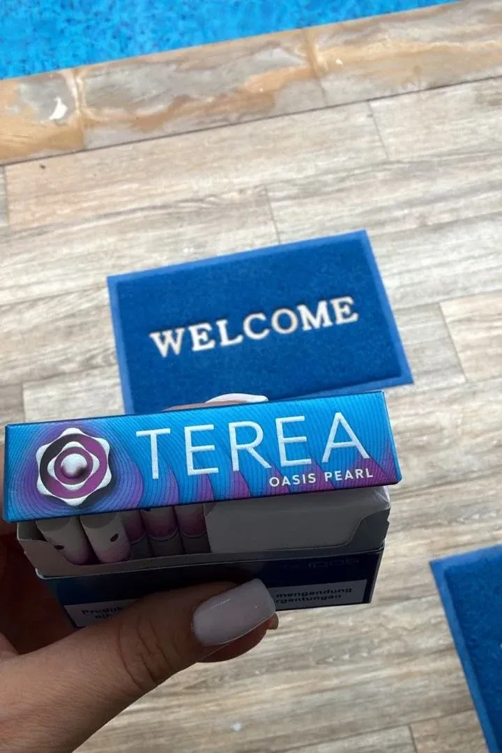 A pack of TEREA Oasis Pearl held over a pool deck with a welcome mat